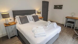 A neatly made bed with pillows, a bedside table with a lamp, a desk with a chair, and a door in a hotel room. - Luxury Apartment, City Break, 4A City Cottage Central Chester (Chester)