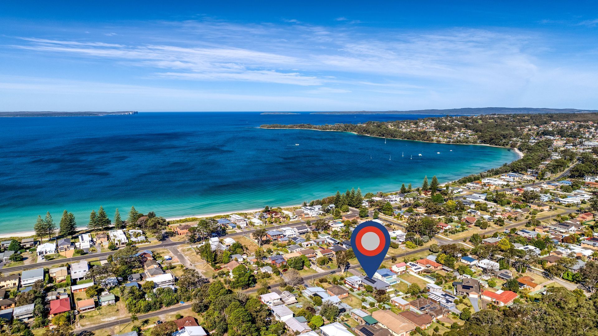 An aerial view of a coastal town with a clear blue sea, a small island, and a dense residential area with houses and roads.