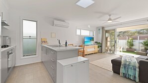 Una cocina moderna con una isla central, un comedor con televisor y un puerta corrediza de vidrio que da a un patio.