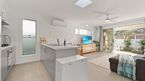 Una cocina moderna con una isla central, un comedor con televisor y un puerta corrediza de vidrio que da a un patio.