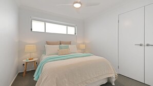 Un dormitorio con cama, dos mesitas de noche, una ventana, ventilador de techo y armario.