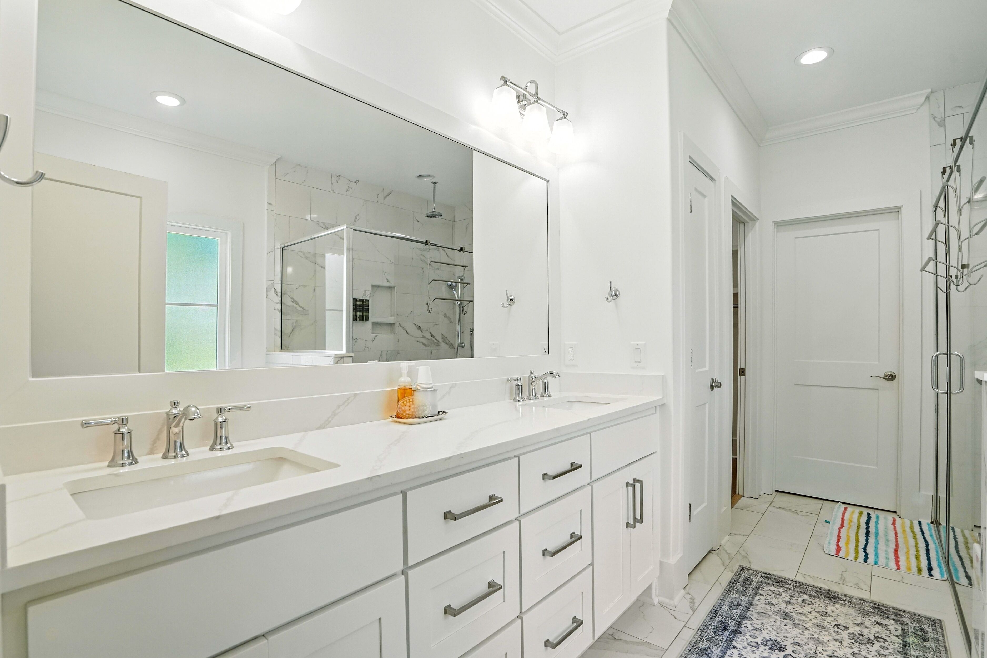 Une salle de bain moderne avec un grand miroir, deux lavabos et un espace douche.