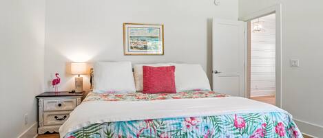 A bedroom with a bed, a nightstand, a lamp, a door, and a wall with a framed picture.