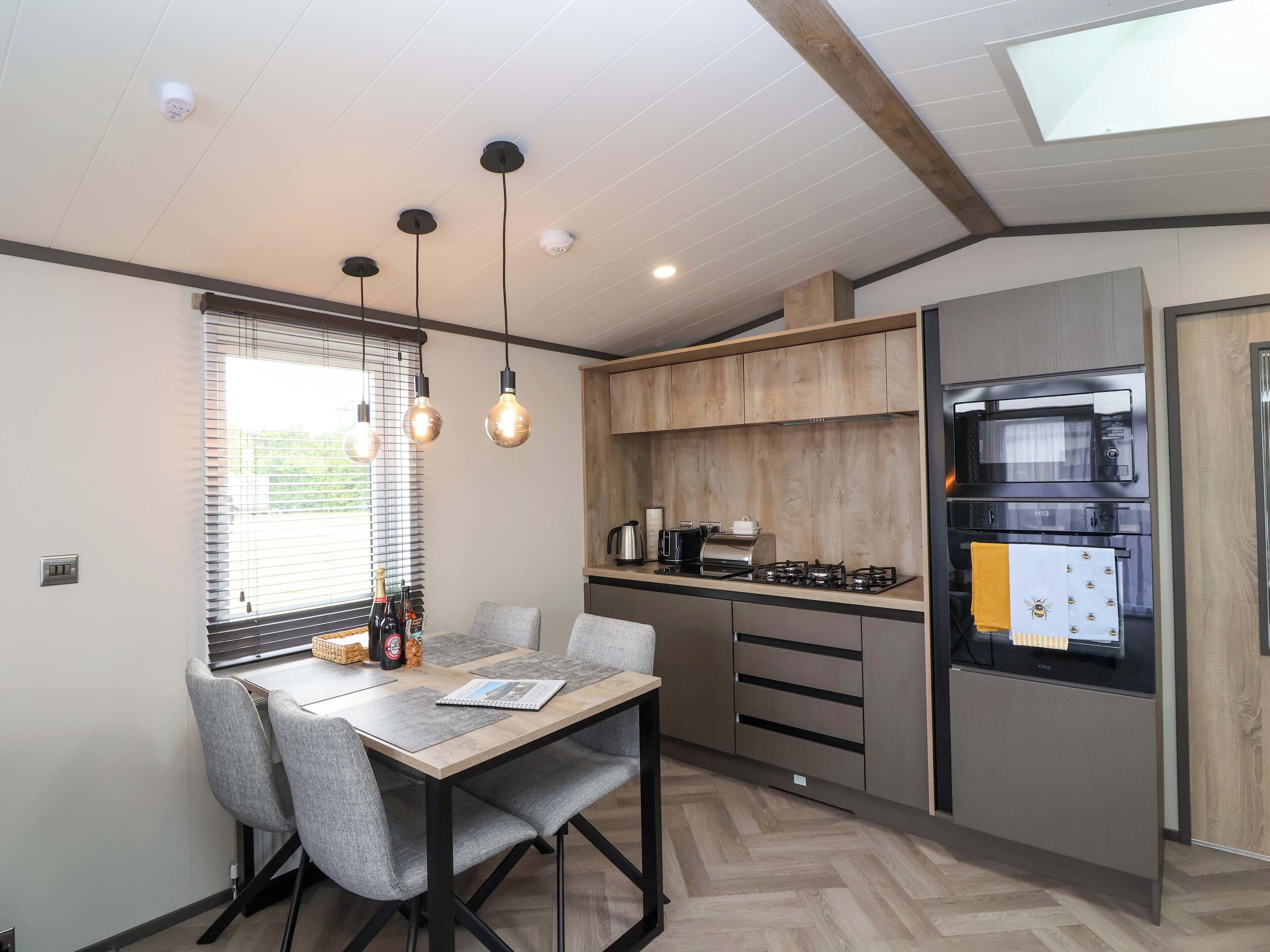 Une cuisine moderne avec un coin repas, comprenant une table en bois, des chaises grises et un four encastré.