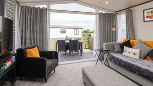 A modern living room with a sofa, armchair, and a TV stand. - Hazelnut Lodge (Chipping Norton)