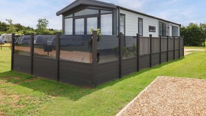 A mobile home with a fenced patio area, a covered outdoor seating area, and a small garden. - Hazelnut Lodge (Chipping Norton)
