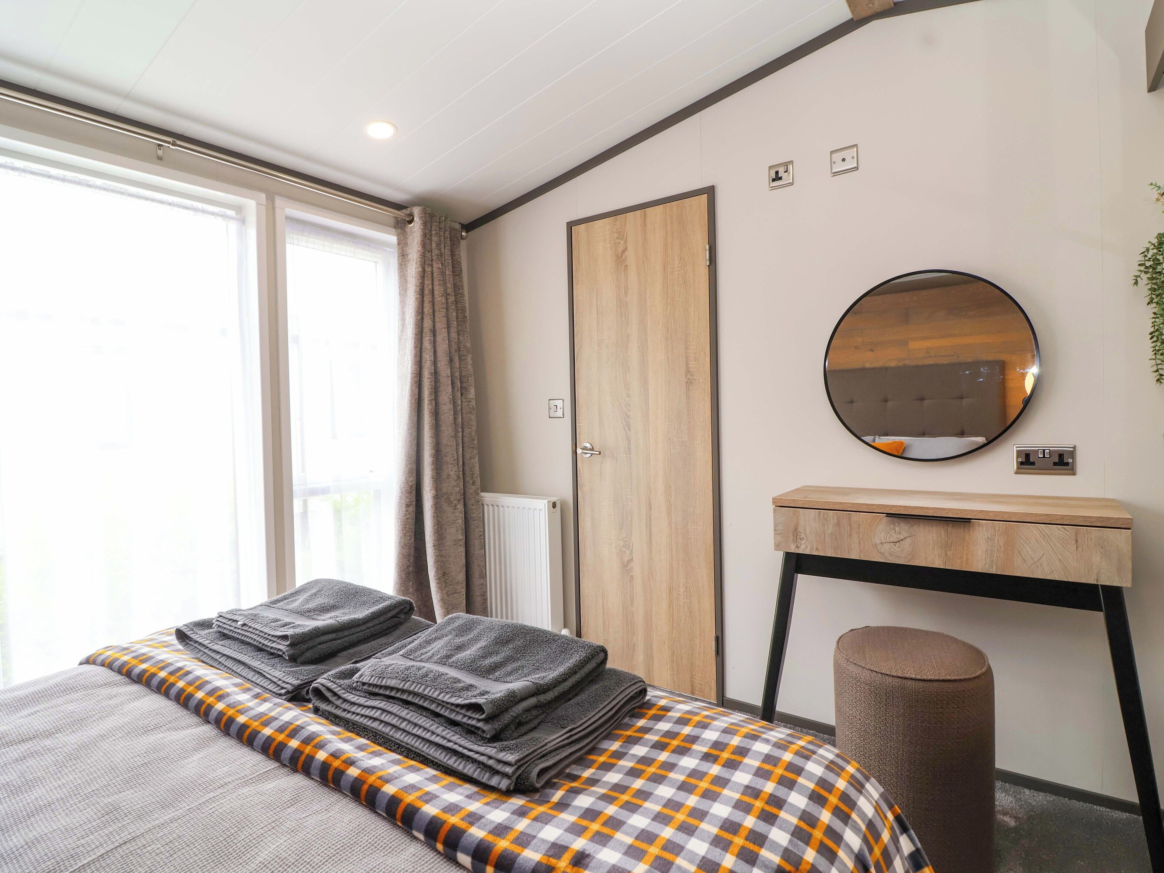 Una habitación de hotel moderna con una cama grande, un armario de madera, un espejo redondo y un escritorio pequeño.