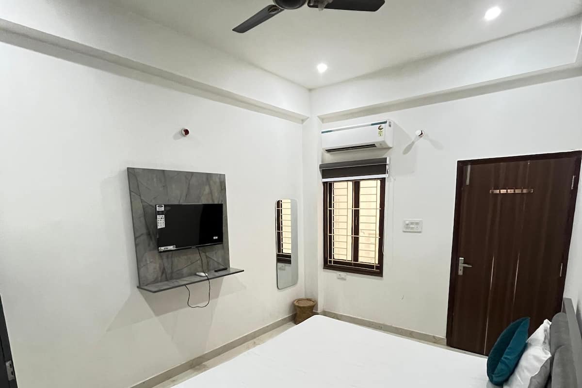 A bedroom with a bed, a ceiling fan, a TV mounted on the wall, a window with bars, and a door.