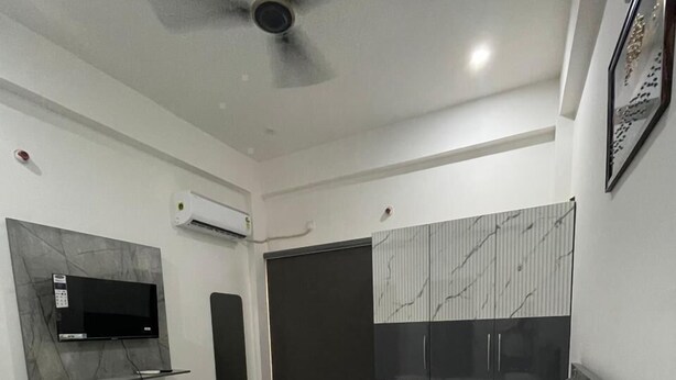 A modern bedroom with a large bed, a ceiling fan, a mounted TV, and a built-in wardrobe. - Hotel Kashi Vaas (Varanasi)