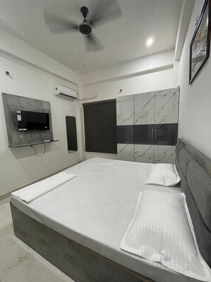 A modern bedroom with a large bed, a ceiling fan, a mounted TV, and a built-in wardrobe. - Hotel Kashi Vaas (Varanasi)