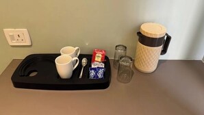 A tray with two white mugs, a spoon, a packet of instant coffee, two small glasses, and a thermos on a table. - Hotel Kashi Vaas (Varanasi)