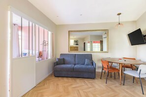 A room with a sofa, dining table, chairs, a TV, and a mirror.