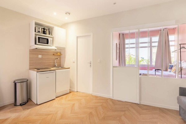 A compact kitchen with a microwave, a small refrigerator, and a trash bin.