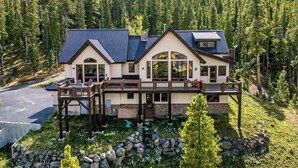 A two-story house with a deck, surrounded by a forest and a rocky garden. - Top Of the World (Crested Butte)