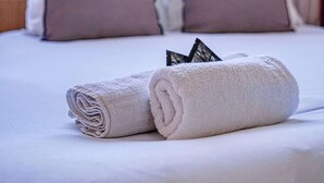 A neatly made bed with a rolled white towel and two pillows, a window with blinds, and a view of a building outside. - Climatisé & fonctionnel – 2BR cœur du 17ᵉ (Unknown)