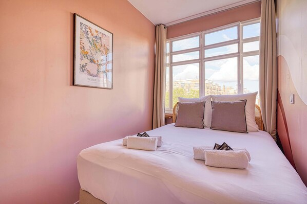 Un cuarto de hotel con una cama grande, una ventana con cortinas y una obra de arte enmarcada en la pared.