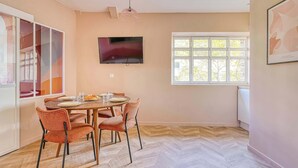 A dining area with a round table, four chairs, a flat-screen TV, and a window with a view of trees. - Climatisé & fonctionnel – 2BR cœur du 17ᵉ (Unknown)
