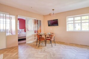 Una habitación con una mesa de comedor, sillas, un televisor montado en la pared y un ventanal grande.