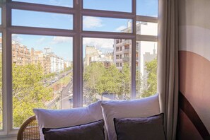 Una habitación con un ventanal grande que da a una vista urbana con edificios y árboles.