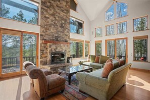 A spacious living area with a stone fireplace, large windows, and a balcony.