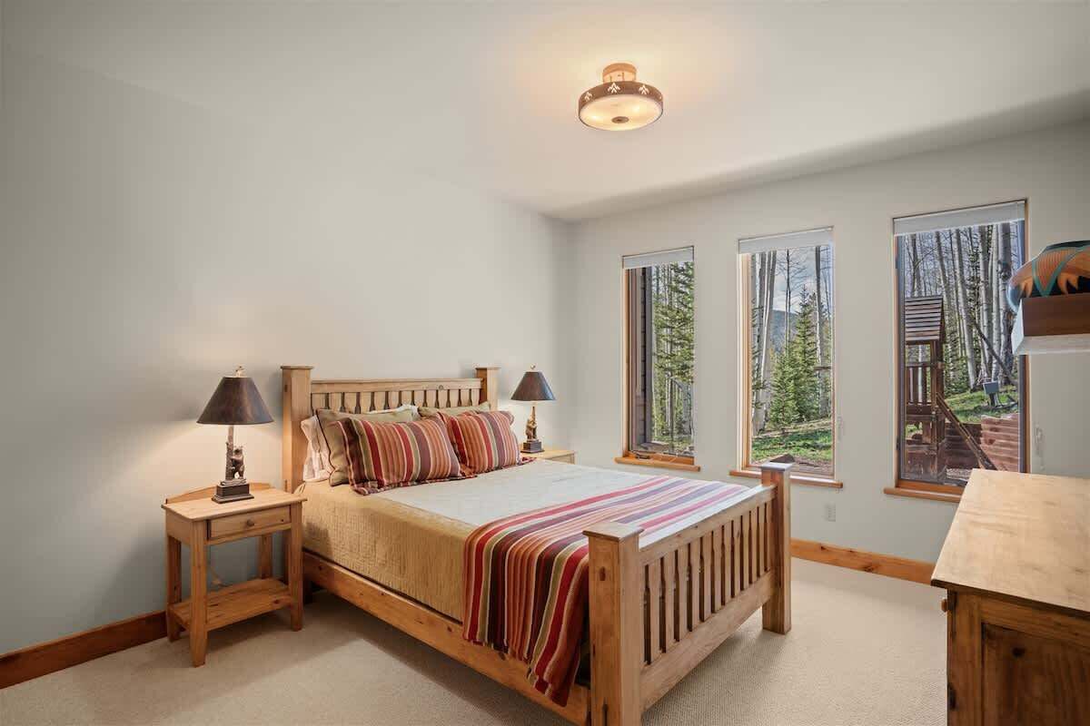 Une chambre à coucher avec un lit en bois, deux tables de chevet, une lampe, une fenêtre donnant sur des arbres et un luminaire au plafond.