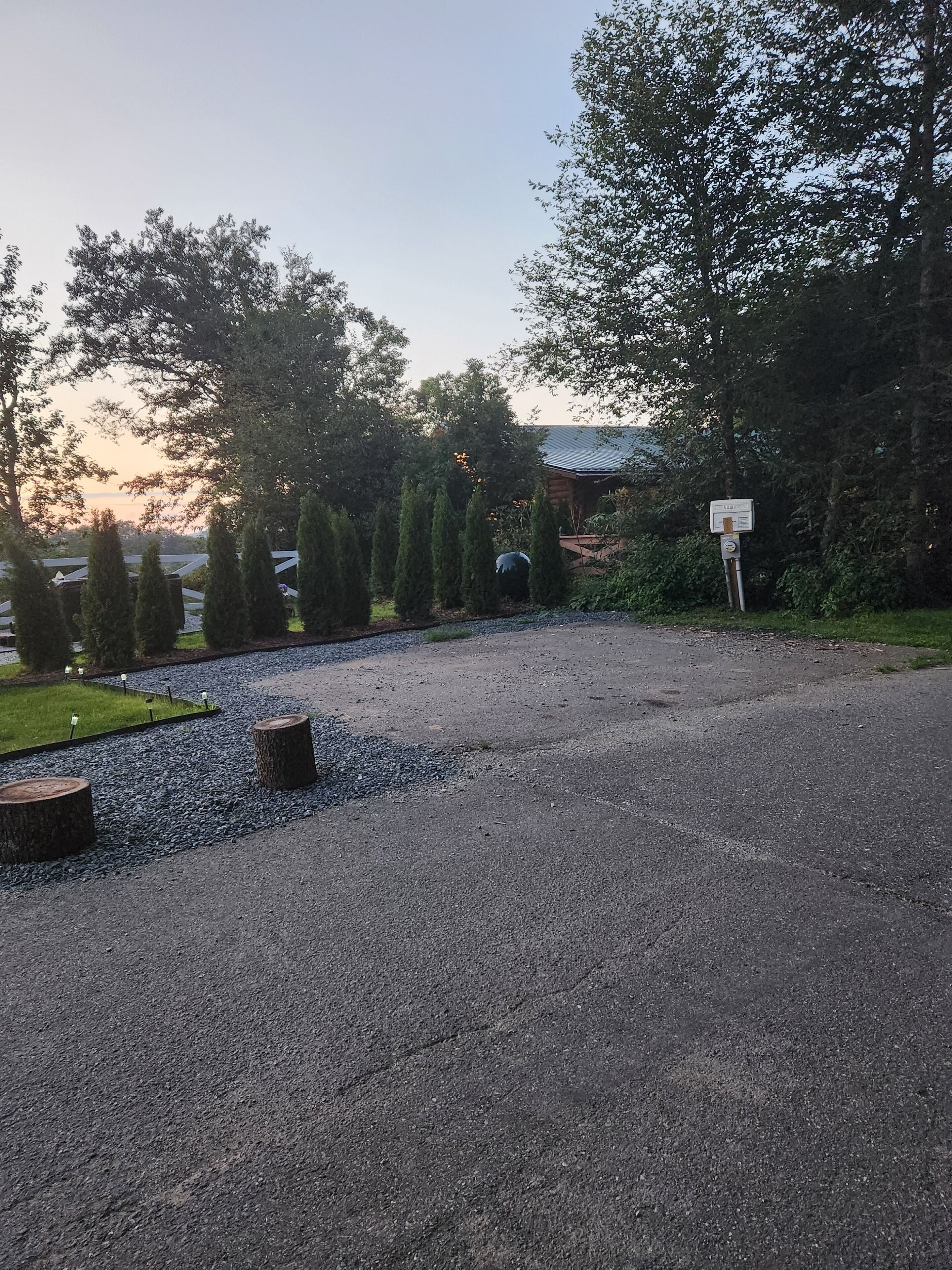 A paved driveway with a wooden post, surrounded by trees and a grassy area.