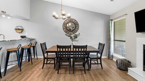 A dining area with a wooden table and chairs, a chandelier, a round mirror, and a small plant on the table.
