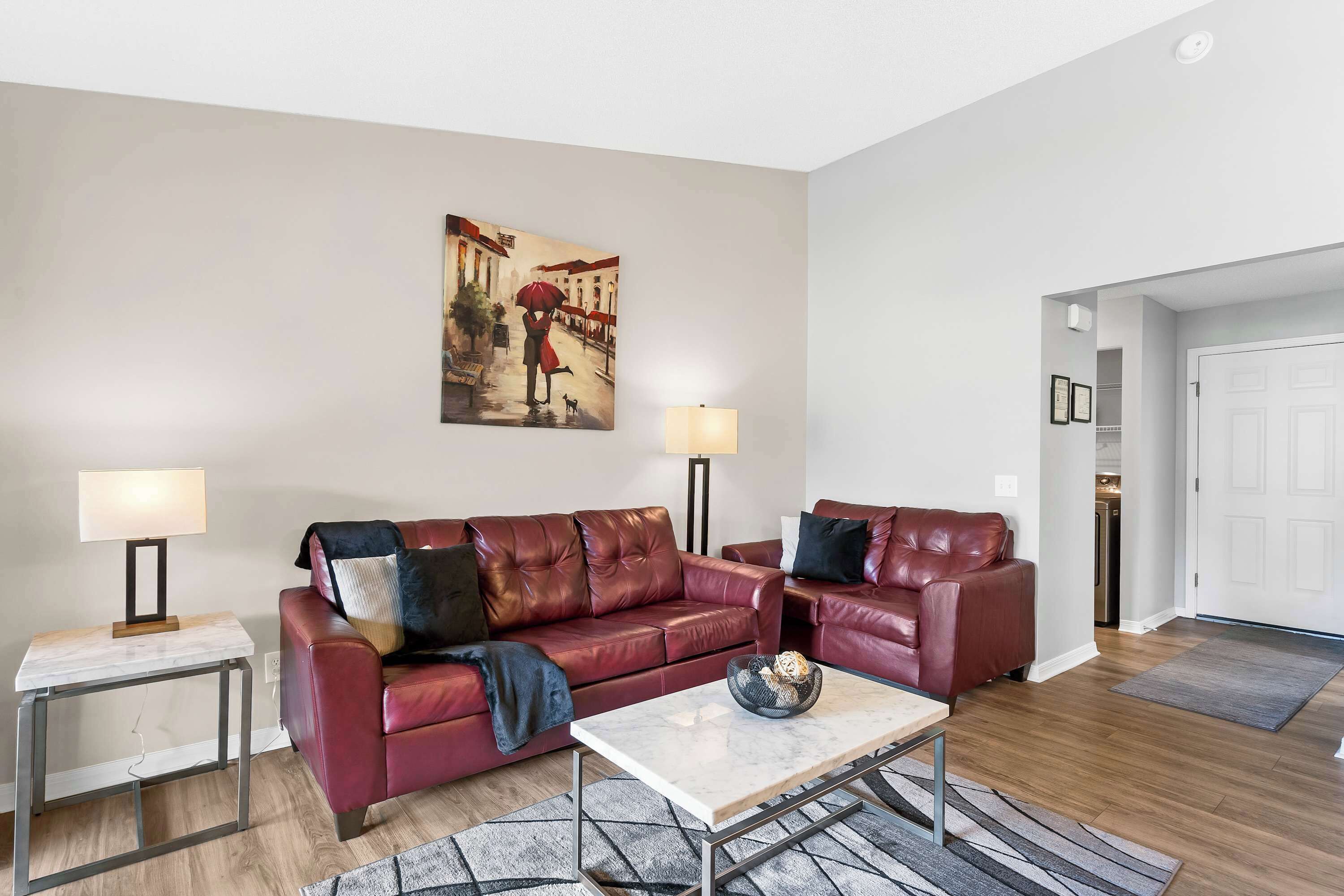 A living room with a red leather sofa, a marble coffee table, and a painting of a street scene.