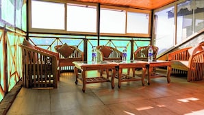 A wooden deck with a table and chairs, large windows, and a view of the mountains. - Shimla Hill View (Shimla)