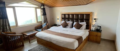 A bedroom with a wooden ceiling, a large bed with a headboard, bedside tables, a window with curtains, and a view of the outdoors.
