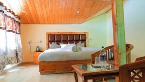 A bedroom with a wooden headboard, a bed with pillows, a nightstand with a kettle, and a glass table with a bottle. - Shimla Hill View (Shimla)