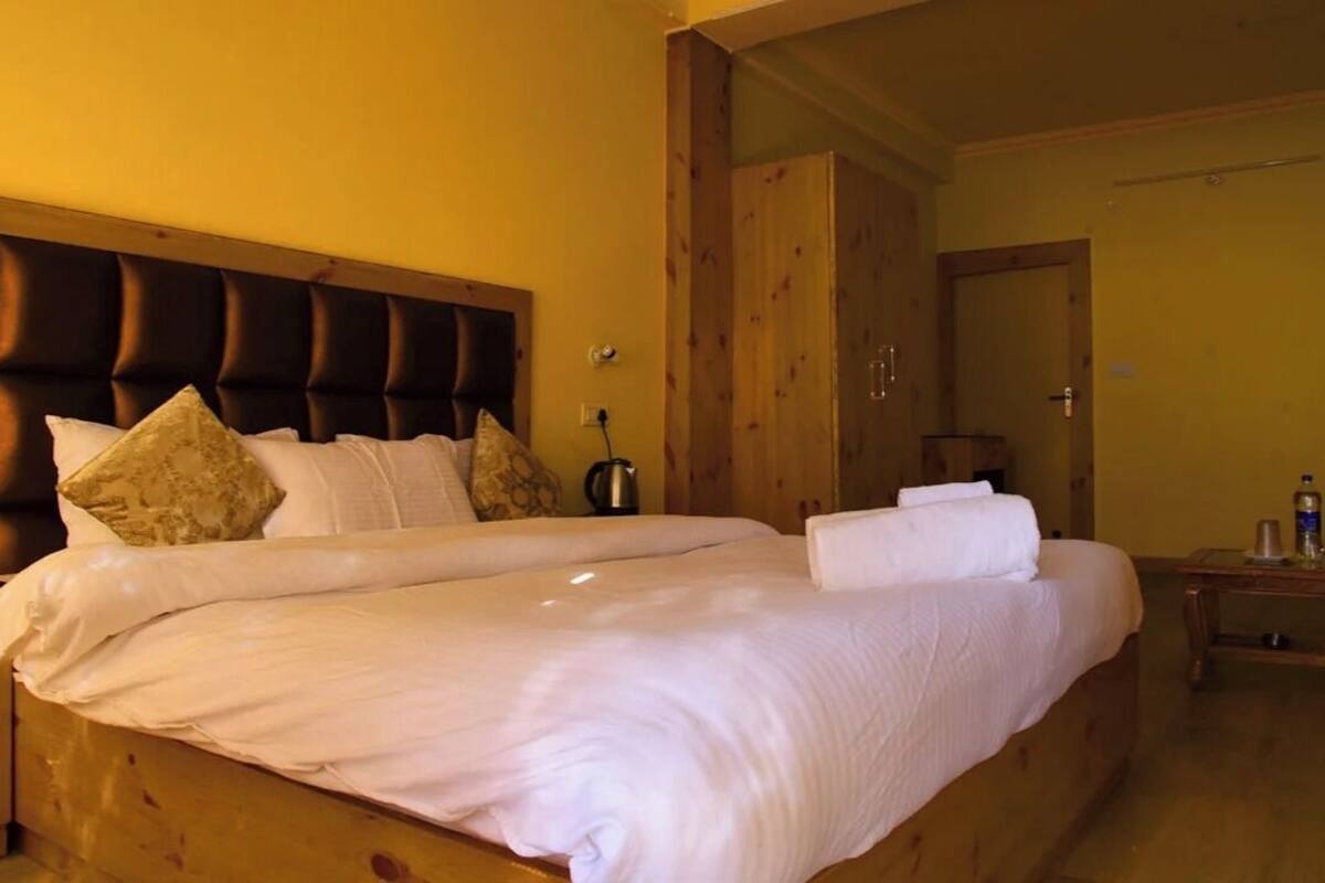 A neatly made bed with a wooden headboard, a wooden wardrobe, and a bedside table with a lamp.