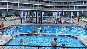A swimming pool with lounge chairs and umbrellas, surrounded by a building with multiple balconies.