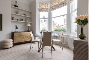 Un coin repas comprenant une table ronde, des chaises blanches, une table avec un plateau en verre et un meuble décoratif.