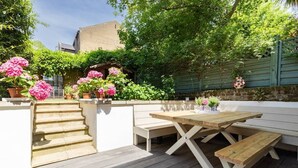A wooden deck with a picnic table and benches, surrounded by potted plants and a stone wall. - Westbourne Park Road Xvii by Onefinestay (London)