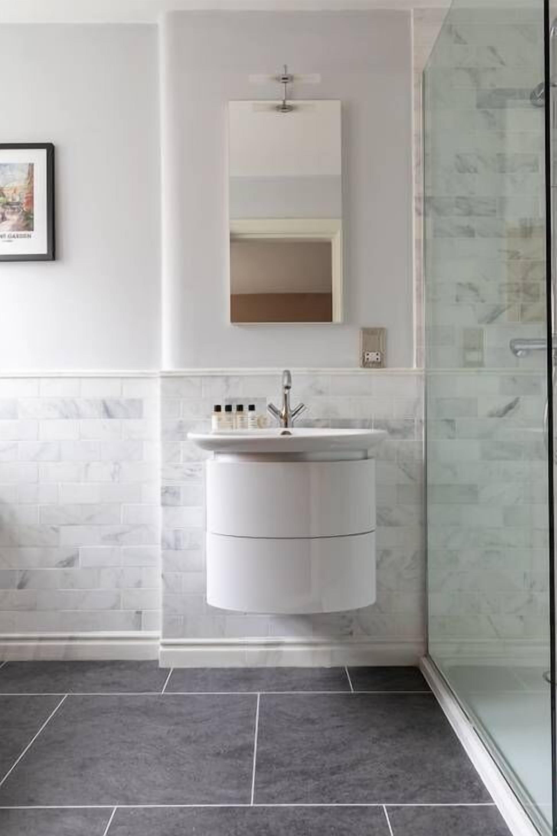 Un baño moderno con tocador blanco, un espejo grande y cabina de ducha de vidrio.