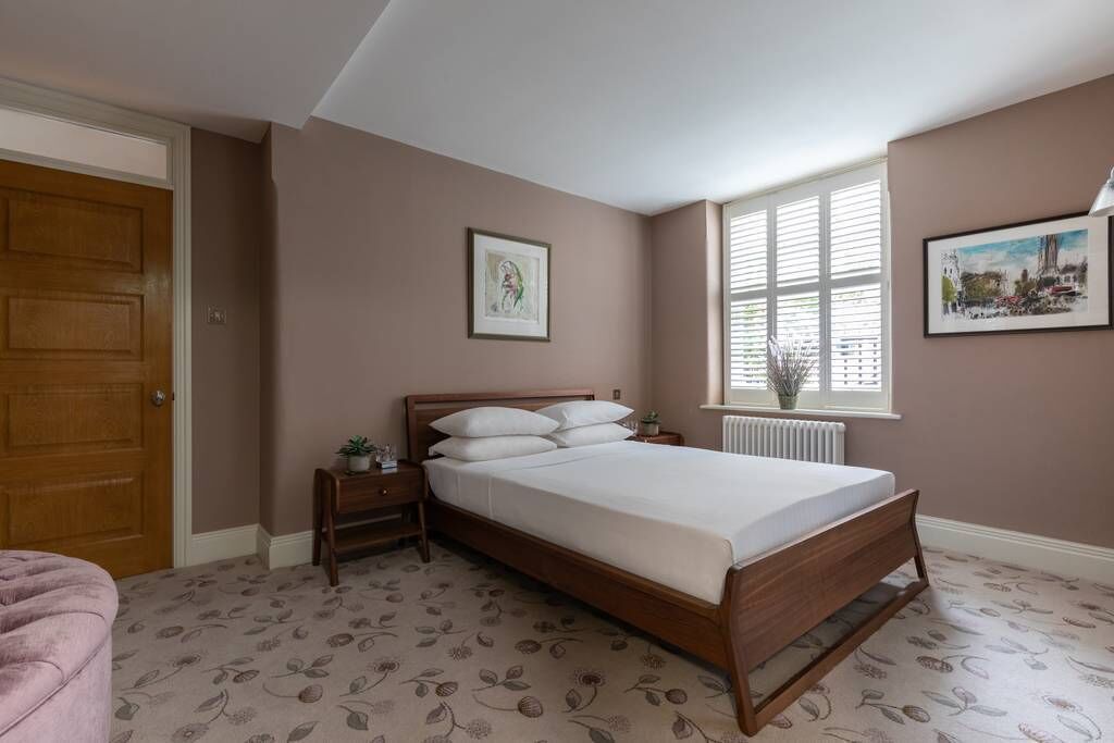 A bedroom with a wooden bed, a nightstand, a window with blinds, and a radiator.