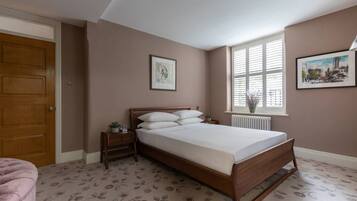 A bedroom with a wooden bed, a nightstand, a window with blinds, and a radiator.