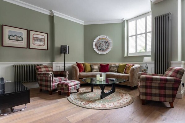 A living room with a sofa, armchairs, a coffee table, and a radiator.