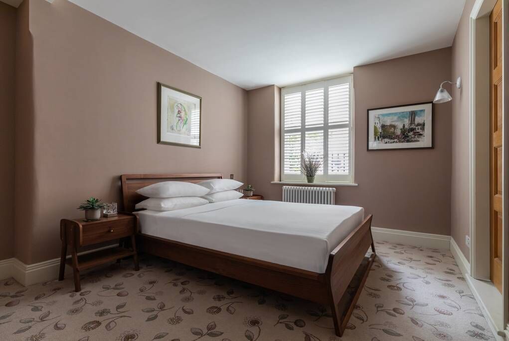 Un dormitorio con una cama de madera, una mesita de noche, una ventana con persianas y dos cuadros en la pared.