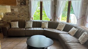 A cozy living room with a large L-shaped sectional sofa, a round coffee table, and a brick wall with a window overlooking greenery.