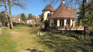 A house with a round tower, surrounded by a well-maintained garden with flowers and trees.