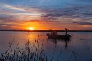 Un atardecer sobre un lago tranquilo con un barco pequeño y una persona pescando.