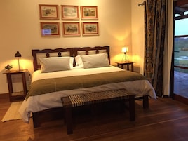 Una cama bien hecha con cabecera de madera, una mesita de noche con lámpara y un banco al pie de la cama.