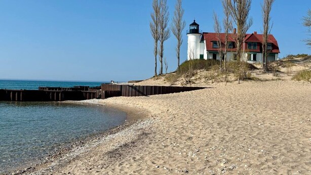 A coastal scene with a lighthouse, a house with a red roof, and leafless trees.