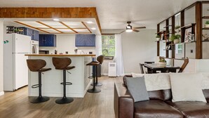 A modern kitchen with bar stools, a dining area with a table and chairs, and a leather sofa.
