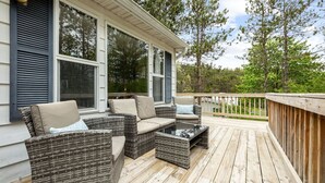 A covered outdoor deck with wicker furniture and a glass door leading to the house.