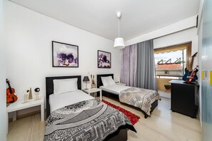 Une chambre d’hôtel avec deux lits, une guitare, une petite table et des œuvres d’art accrochées au mur.