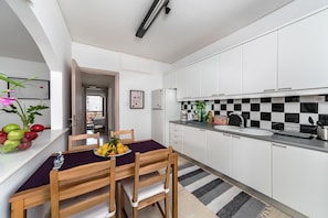 A modern kitchen with white cabinets, a black and white checkered backsplash, and a dining area with a purple tablecloth.