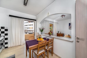 Un espace repas moderne avec une table dressée pour quatre personnes, un miroir au-dessus de la table et une vue sur le balcon et les bâtiments environnants.